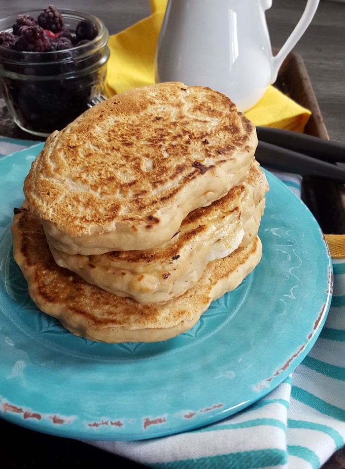 Stack of 3 thick pancakes on a plate with a small jar of berries behind it.