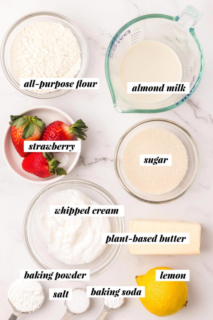 All of the ingredients needed for making a vegan strawberry shortcake recipe with biscuits and whipped cream. Each ingredient is labelled with text.