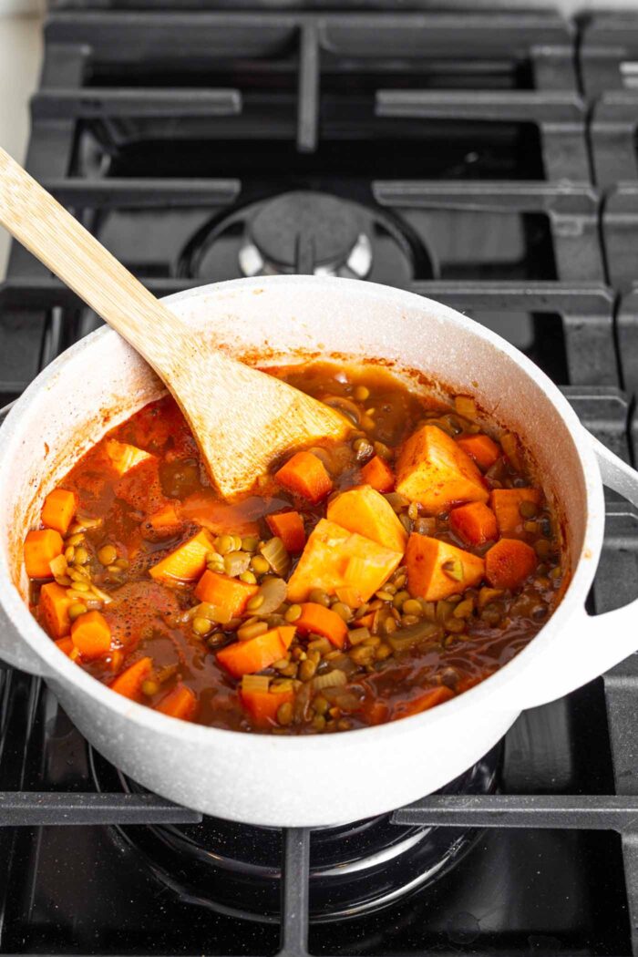 A thick tomato lentil stew cooking on a gas range stove.