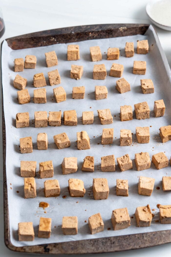 Cubed tofu on a baking pan lined with parchment paper.