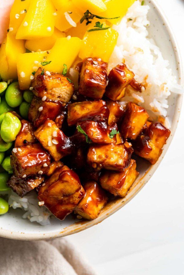 Close up of sweet and spicy tofu in a bowl with rice, mango and edamame.
