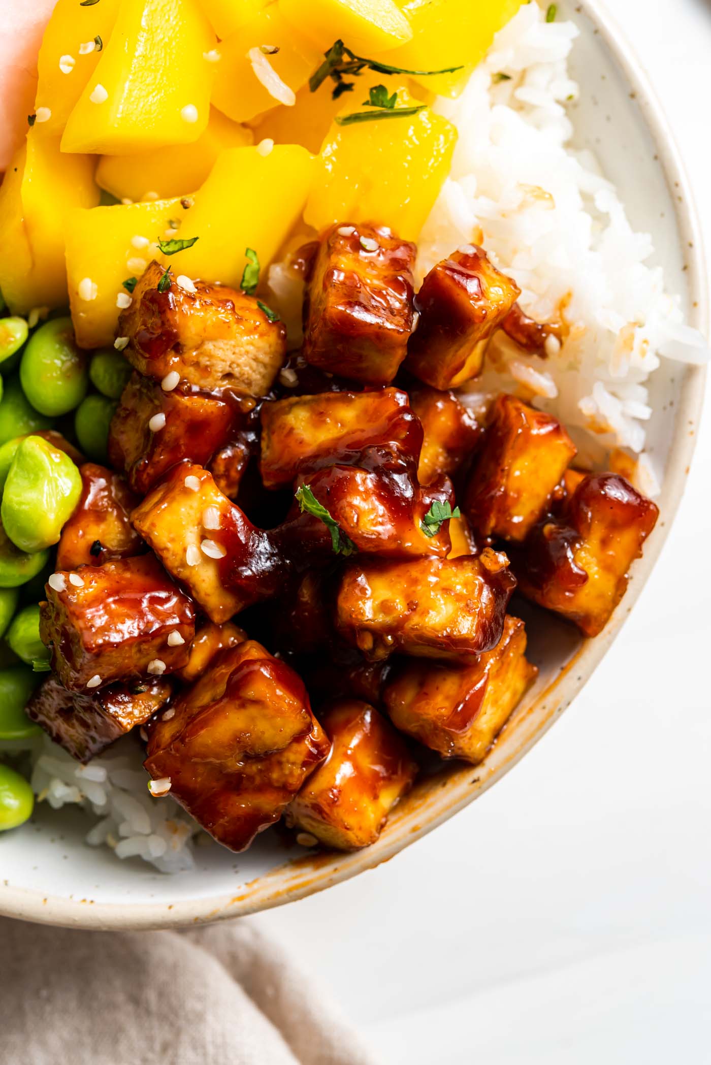 Close up of sweet and spicy tofu in a bowl with rice, mango and edamame.