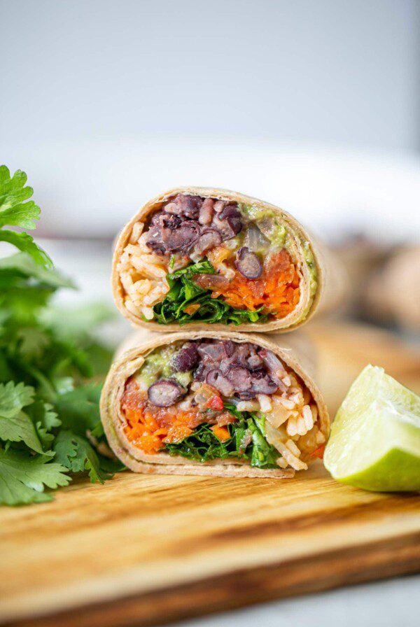Two halves of a black bean burrito stacked on top of each other on a cutting board.