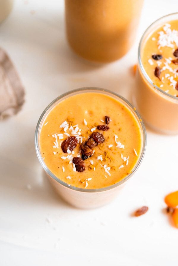 Creamy carrot smoothie in a glass topped with a few raisins.