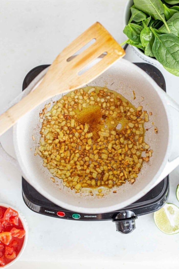 Spices, onions, garlic and ginger cooking in a pot with a wooden spoon.