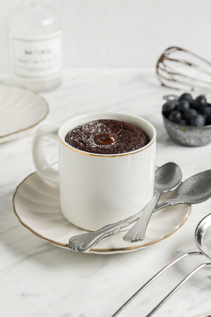 Chocolate mug cake on a small plate with 2 spoons resting on plate.
