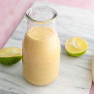 Creamy mango coconut smoothie in a glass milk jar on a marble cutting board with two lime halves beside the glass.