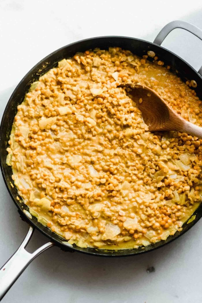 A creamy red lentil dahl in a skillet with a spoon.