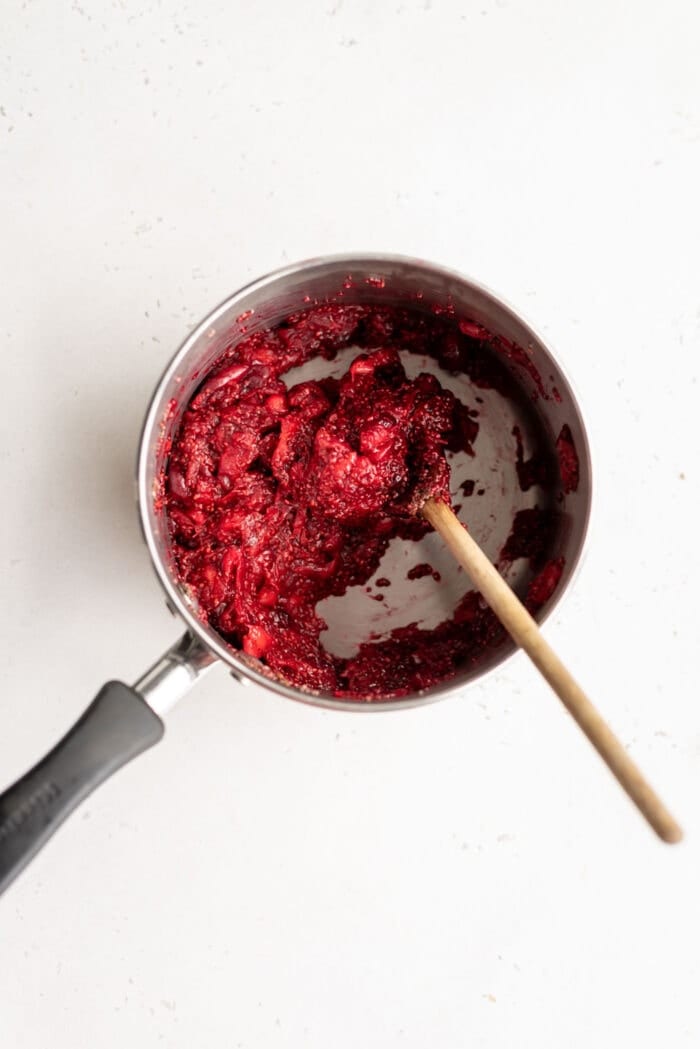 Thick cranberry chia jam in a small saucepan with a wooden spoon.