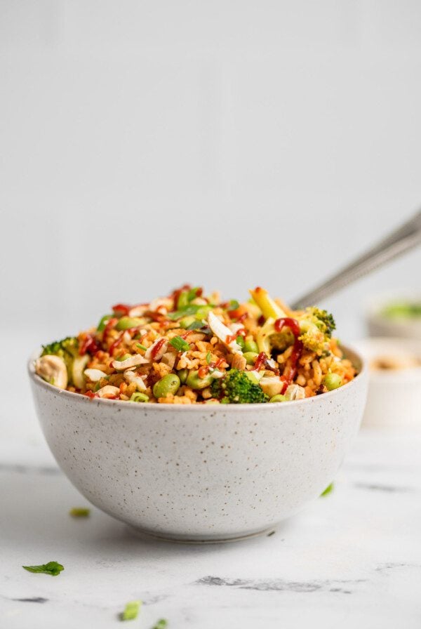 Bowl of fried rice with broccoli, carrot, edamame and green onion topped with chopped cashews.