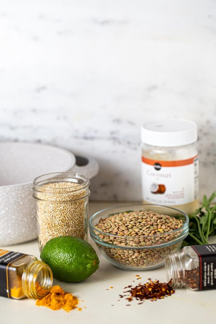 A bowl of lentils, container of quinoa, a lime and a few containers of spices sitting on a counter top.