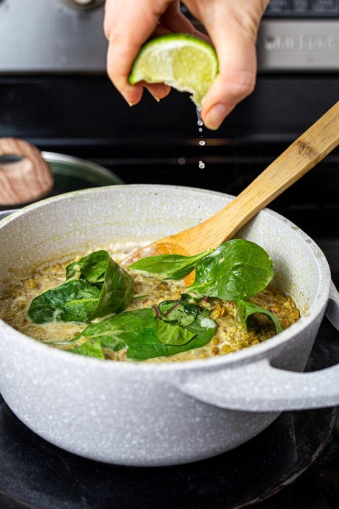 Squeezing lime juice into a pot of lentils, quinoa and spinach on the stovetop.