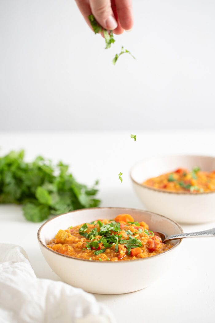 Hand spinkling cilantro over a bowl of lentil soup.