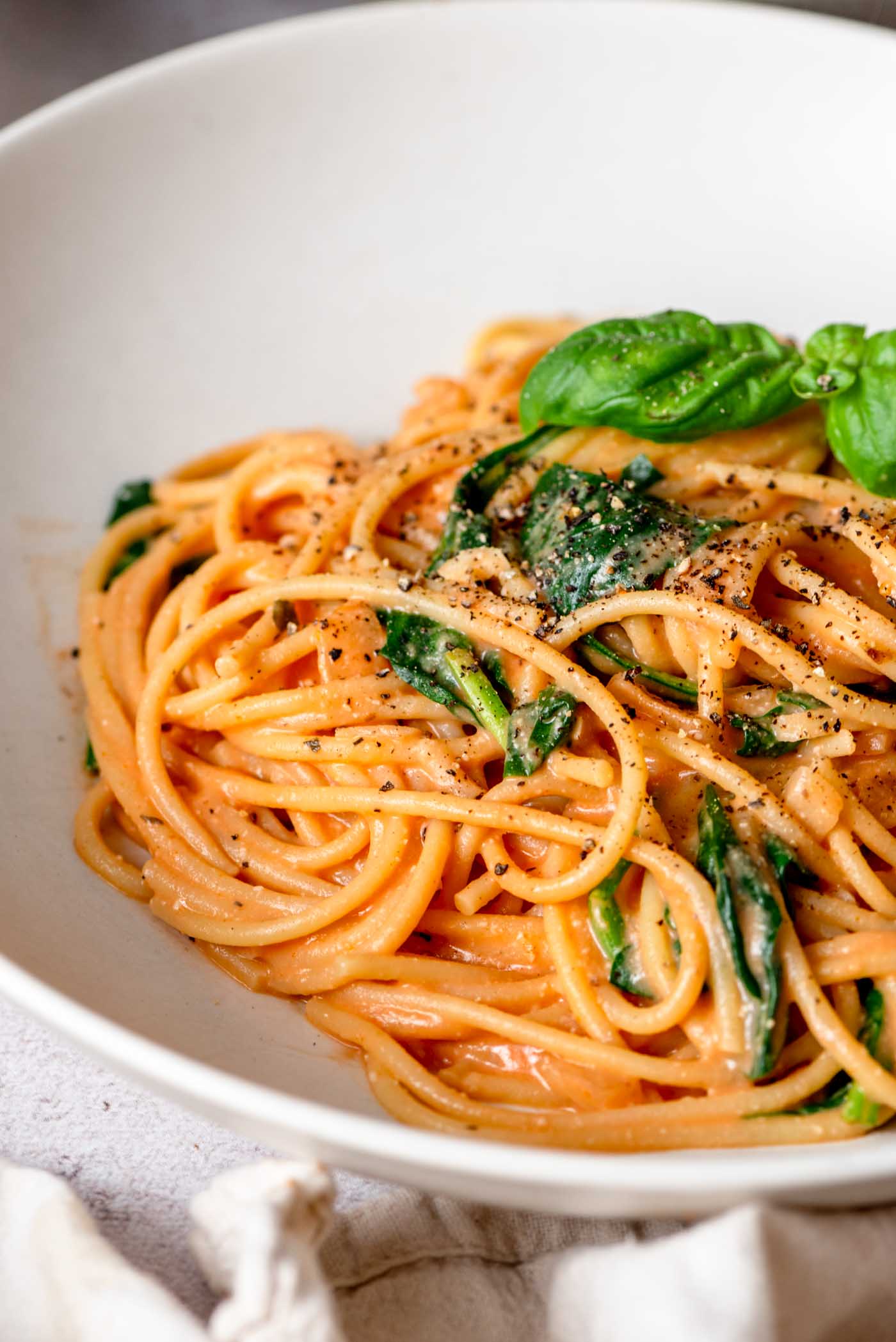 Bowl of creamy tomato pasta topped with a few leaves of fresh basil and fresh cracked black pepper.