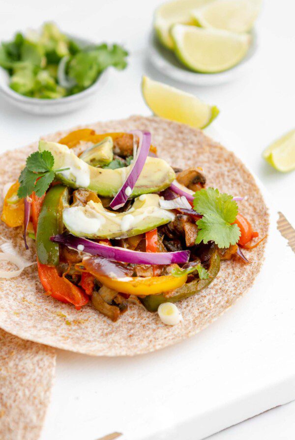 Tortilla filled with bell peppers, onion and avocado on a cutting board.