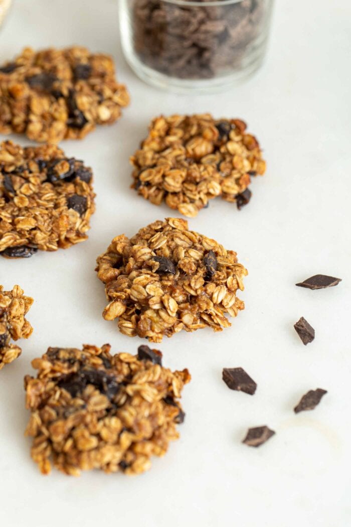 Oatmeal chocolate chip cookies sitting on a white surface with a few chocolate chips scattered around them.