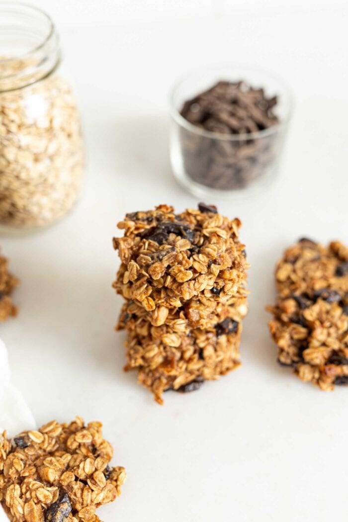 Stack of a few oatmeal chocolate chip cookies with more cookies and jars of ingredients in the background.