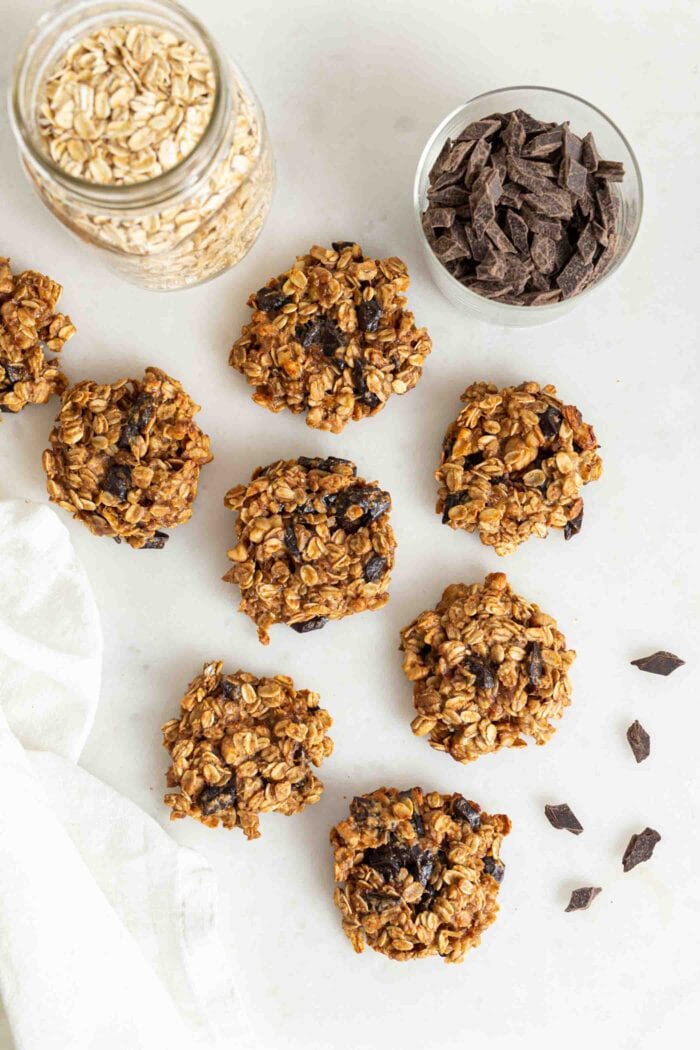 Oatmeal chocolate chip cookies on a white surface beside a jar of chocolate chips and jar of oats.