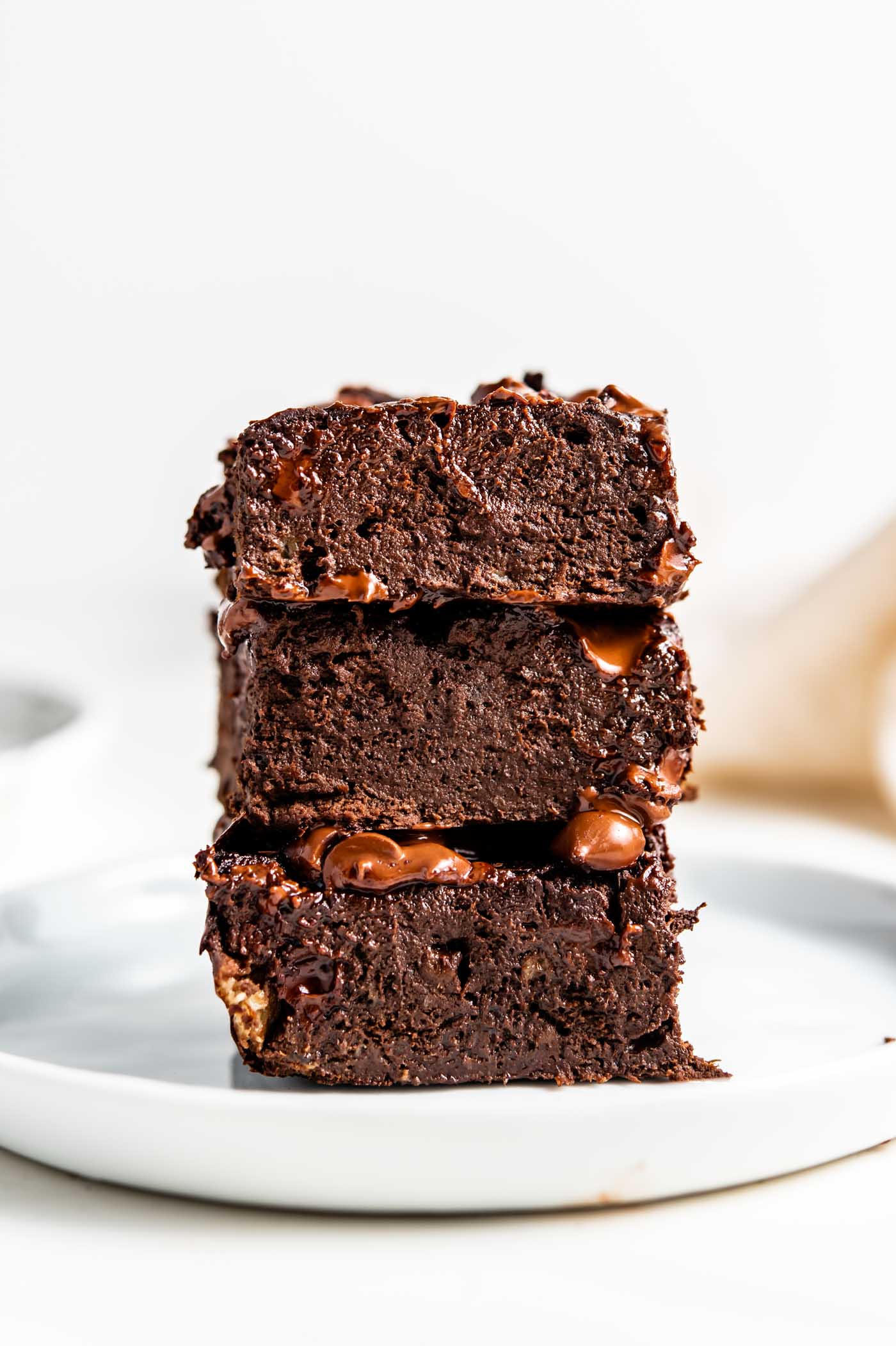 Stack of 3 chocolate brownies on a small white plate.