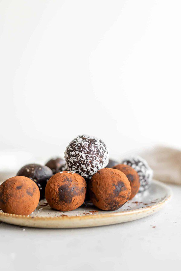 A plate of raw brownie balls rolled in cocoa powder and shredded coconut.