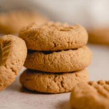 A stack of 3 small peanut butter cookies with another cookie leaning against the stack. The cookies have a crisscross pattern on top.