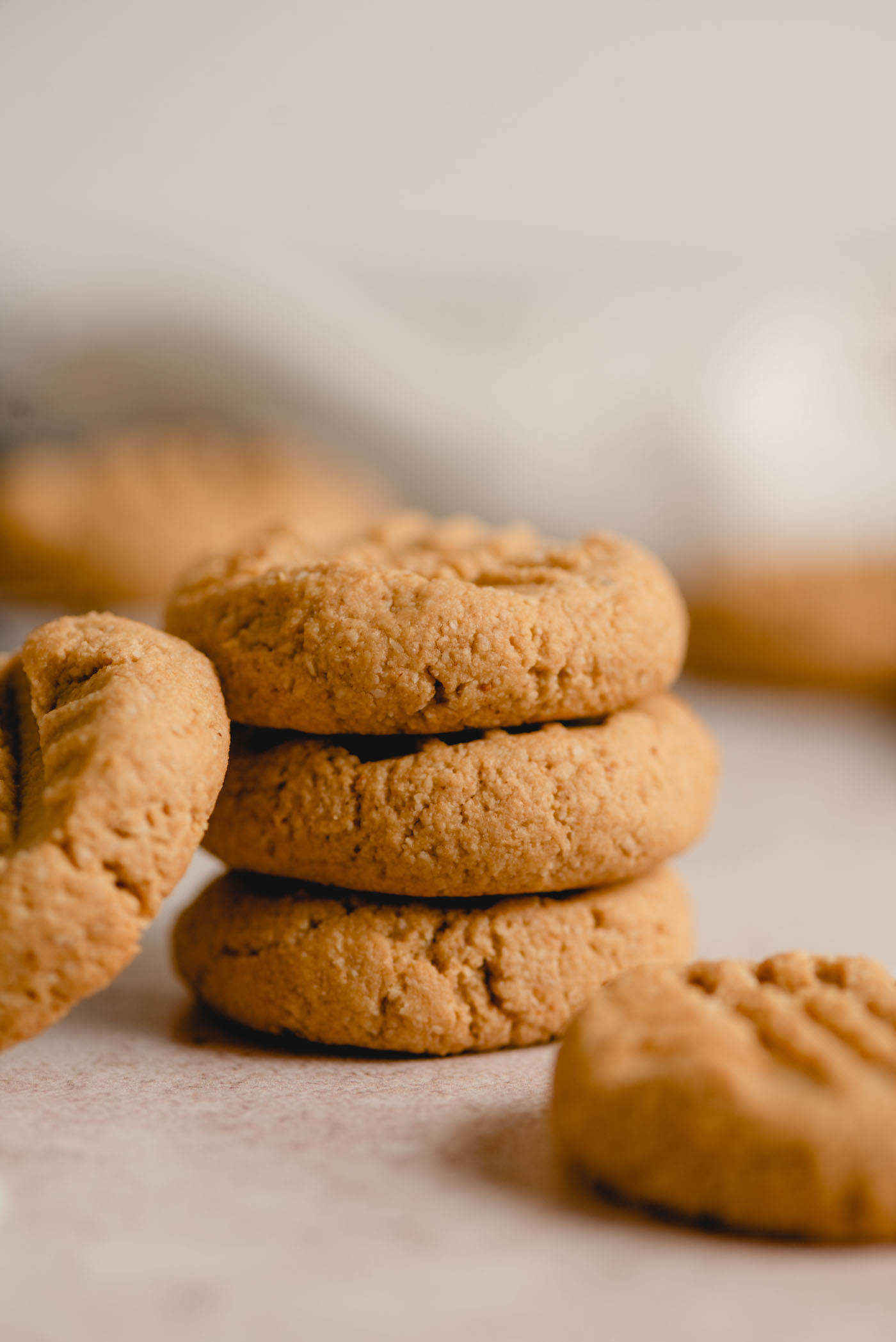 A stack of 3 small peanut butter cookies with another cookie leaning against the stack. The cookies have a crisscross pattern on top.