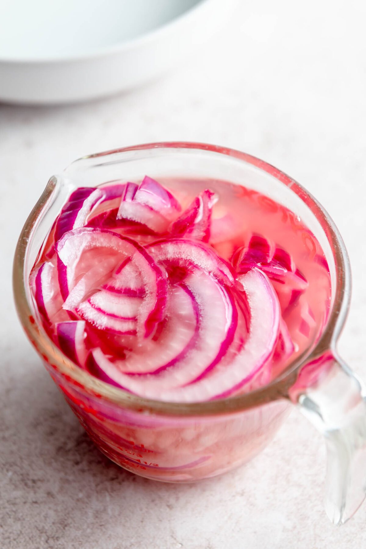Thinly sliced pickled red onions in glass measuring cup.