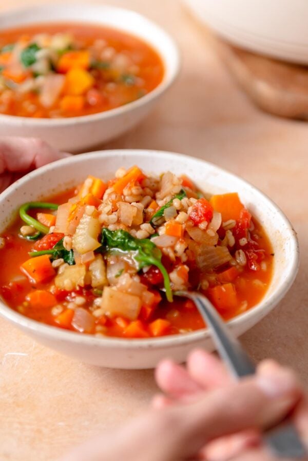 Spoon in a bowl of vegetable barley soup with sweet potato and spinach.