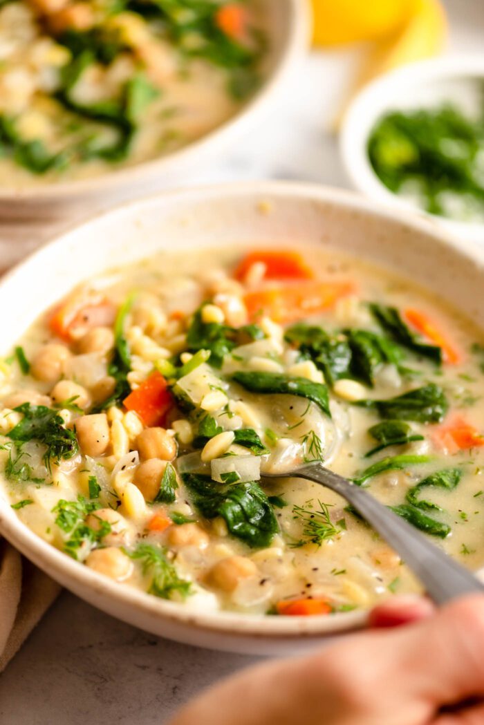 Lifting a spoonful of lemon chickpea orzo soup from a bowl.