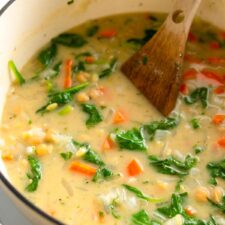 Large soup pot of lemon orzo soup with spinach and chickpeas. A wooden spoon rests in the pot.