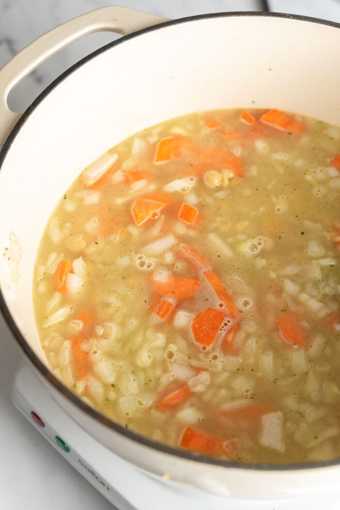 Brothy orzo chickpea lemon soup cooking in a large soup pot.