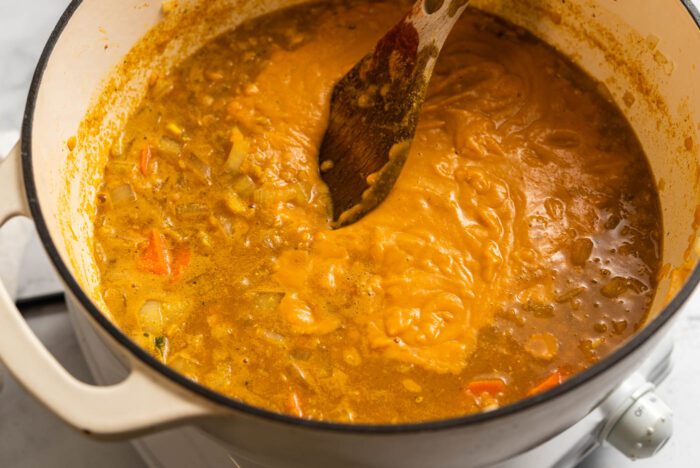 Half blended red lentil lemon soup in a soup pot with a wooden spoon.