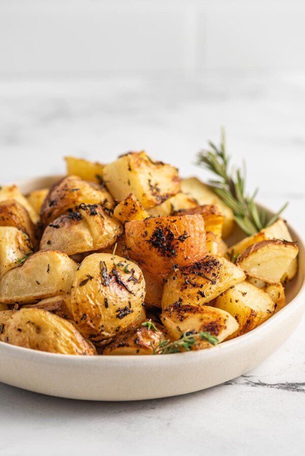 Close up of a bowl of rosemary lemon roasted potatoes with a sprig of rosemary in the bow.