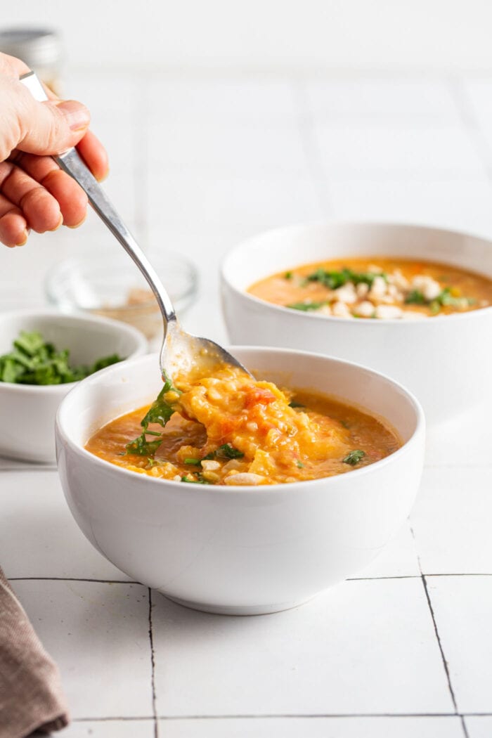 Hand using a spoon to take a spoonful of mulligatawny from a bowl.