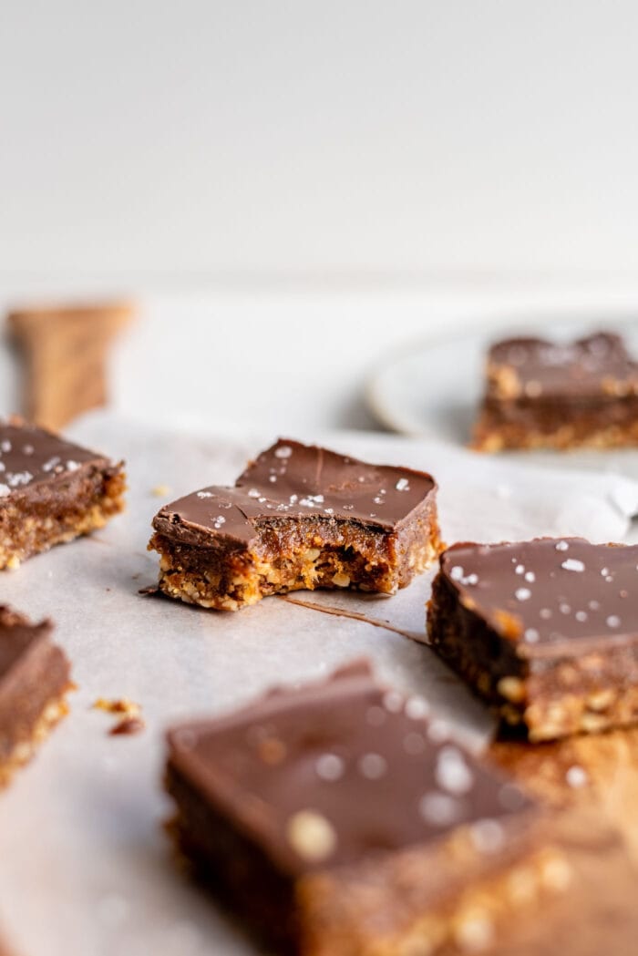 A chocolate caramel bar with a bite taken out of it on a cutting board.