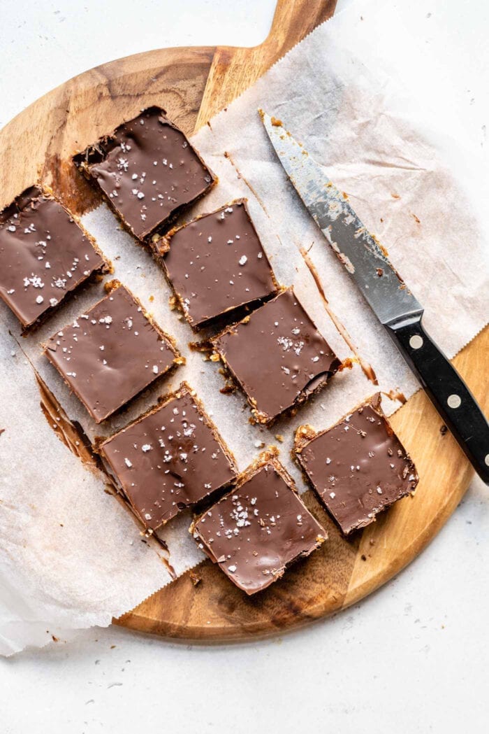 8 chocolate caramel bars on a cutting board with a knife.