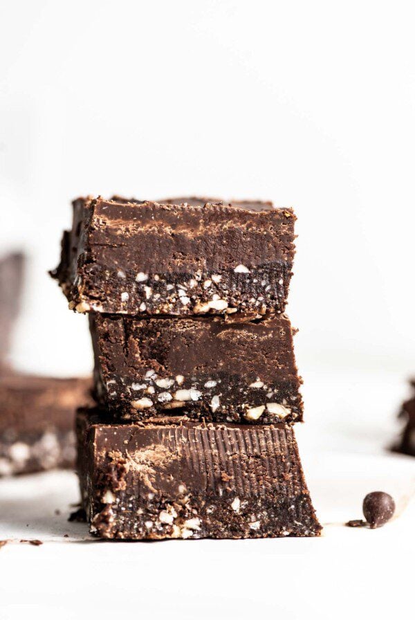Close up of a stack of 3 triple layered chocolate squares with cashews pieces in the bottom layer.