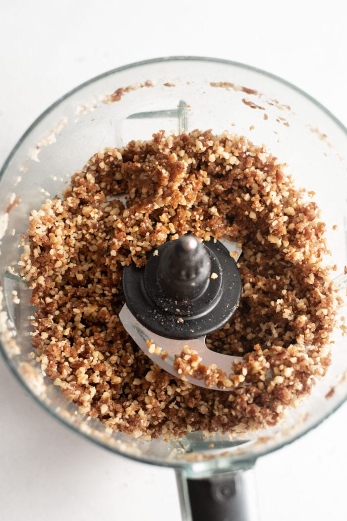 Crumbly date and walnut dough in a food processor container.