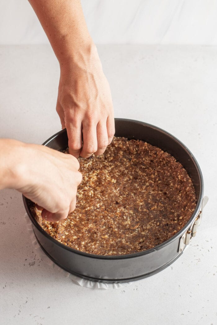 Hands working a doughy crust into a springform pan.