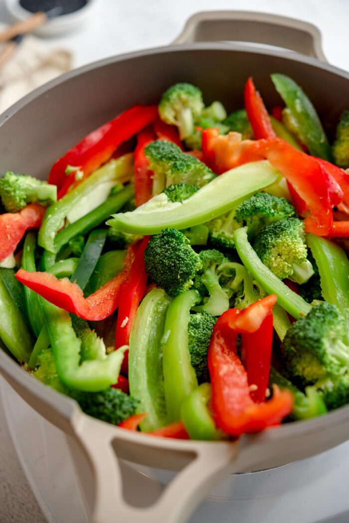 Bell pepper, green onion and broccoli cooking in a large skillet.