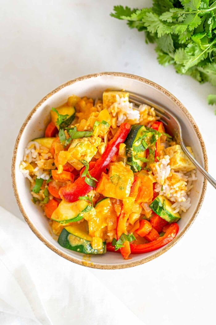 A bowl of tofu vegetable curry over rice with cilantro beside it.