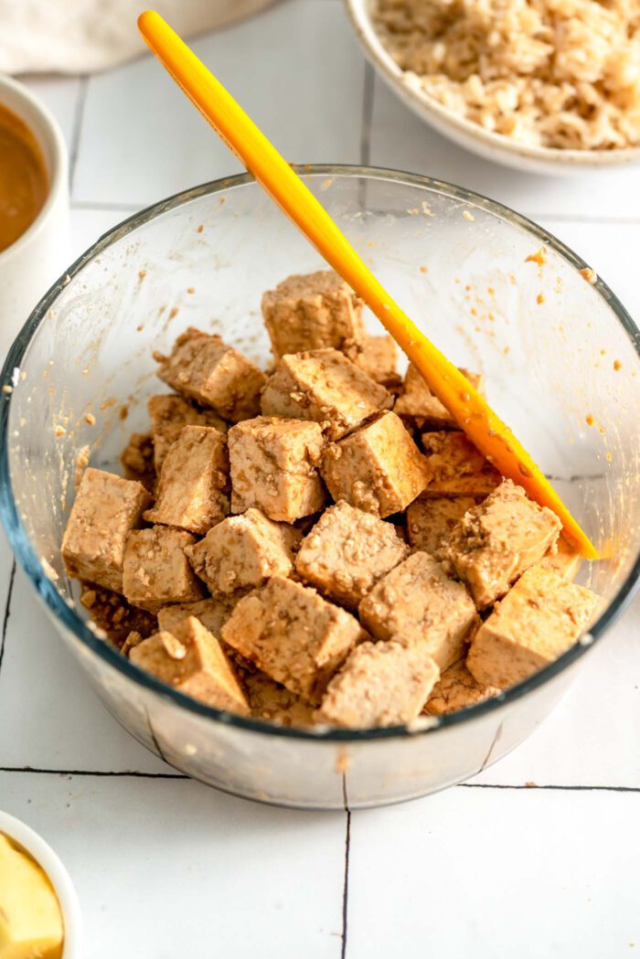 Cubed tofu marinating in sauce in a round glass container.
