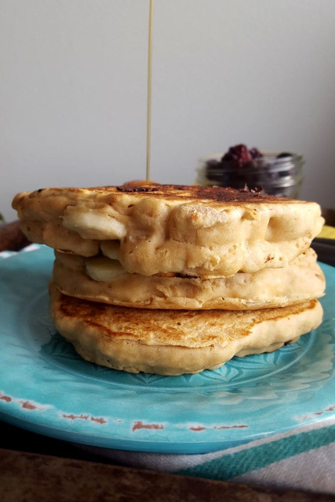 Drizzling maple syrup onto a stack of pancakes on a plate.