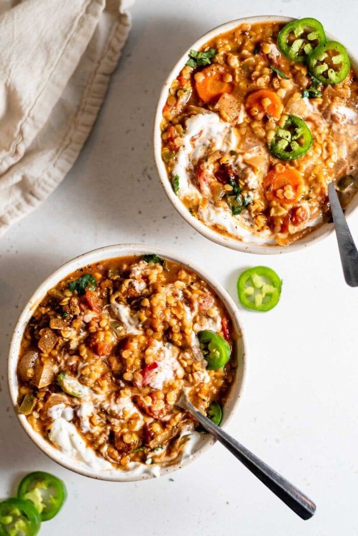 Two bowls of red lentil chili topped with sour cream and sliced jalapeños.