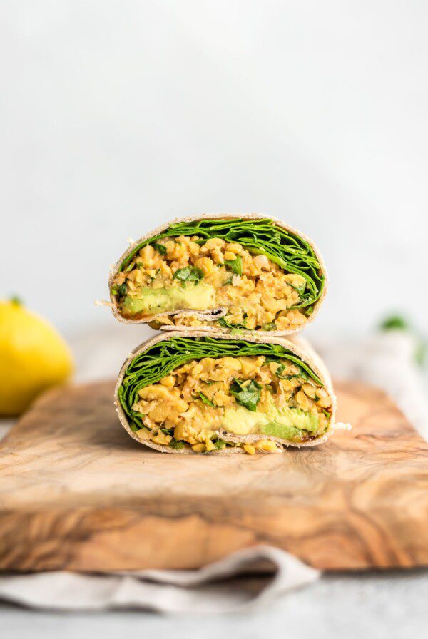 Two stacked halves of a chickpea salad, avocado and spinach wrap cut on a cutting board.