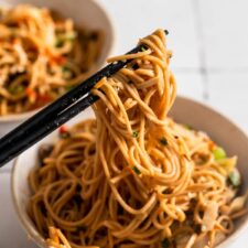 Hand using a set of chopsticks in a small bowl of miso noodles with cabbage and mushrooms.