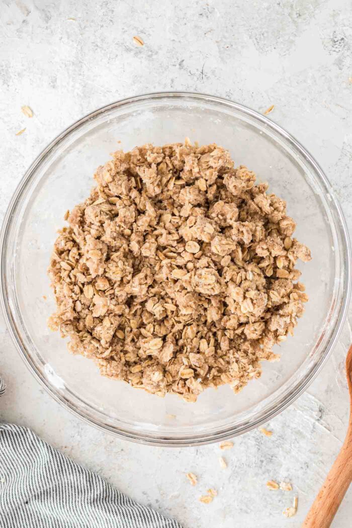 An oatmeal crumble mixture with brown sugar mixed up in a glass mixing bowl.