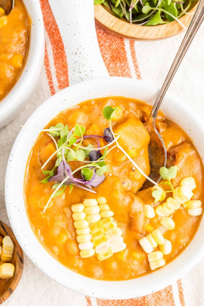 Close up overhead view of a bowl of summer corn chowder with sun dried tomato and potato in it. The soup is topped with corn kernels and a few micro greens.