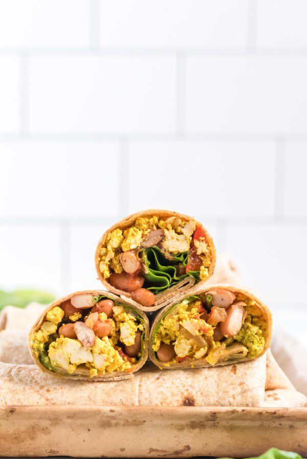 Three breakfast burritos on a cutting board.