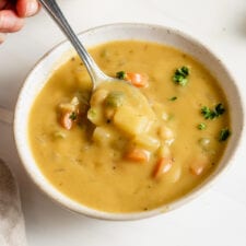 Hand using a spoon to take a spoonful of vegan chickpea soup from a bowl.